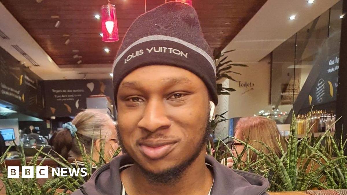 Khaleed Oladipo wearing a black hat and zip-up jacket, smiling.