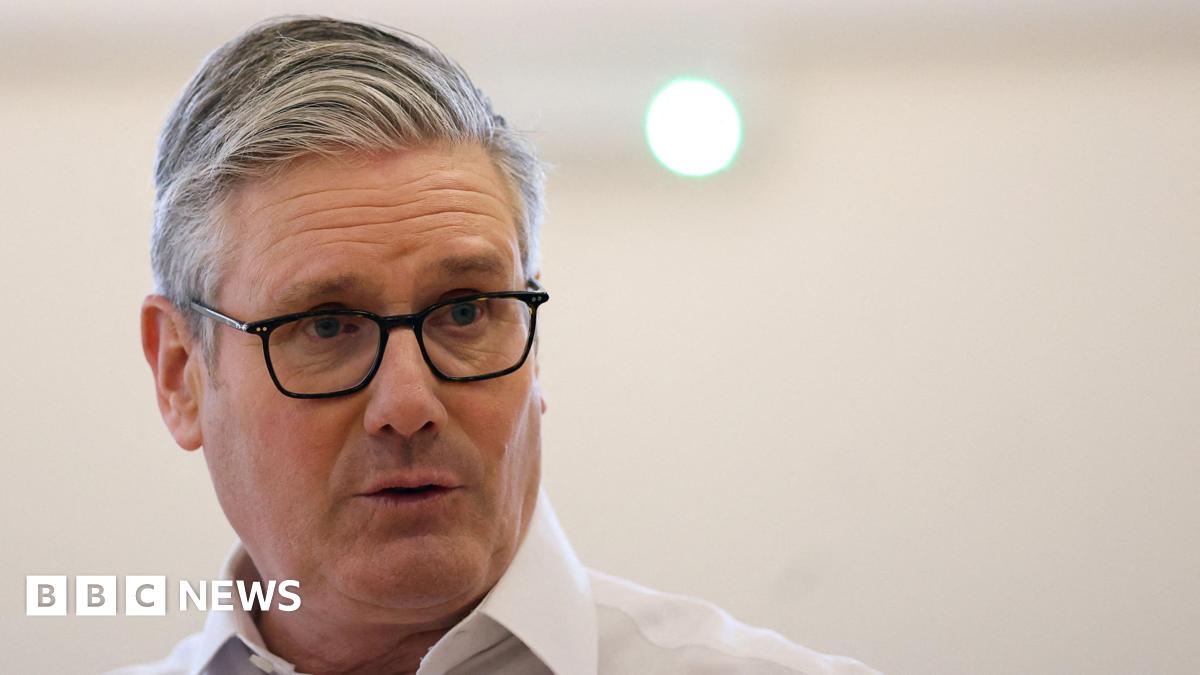 A close-up shot of Keir Starmer, wearing black glasses and a white shirt