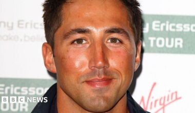 Two woman in front of a green shop, with someone on a ladder in the background. The woman on the left is wearing a blue shirt with brown dots, and the lady on the right is wearing a brown long-sleeve t-shirt.