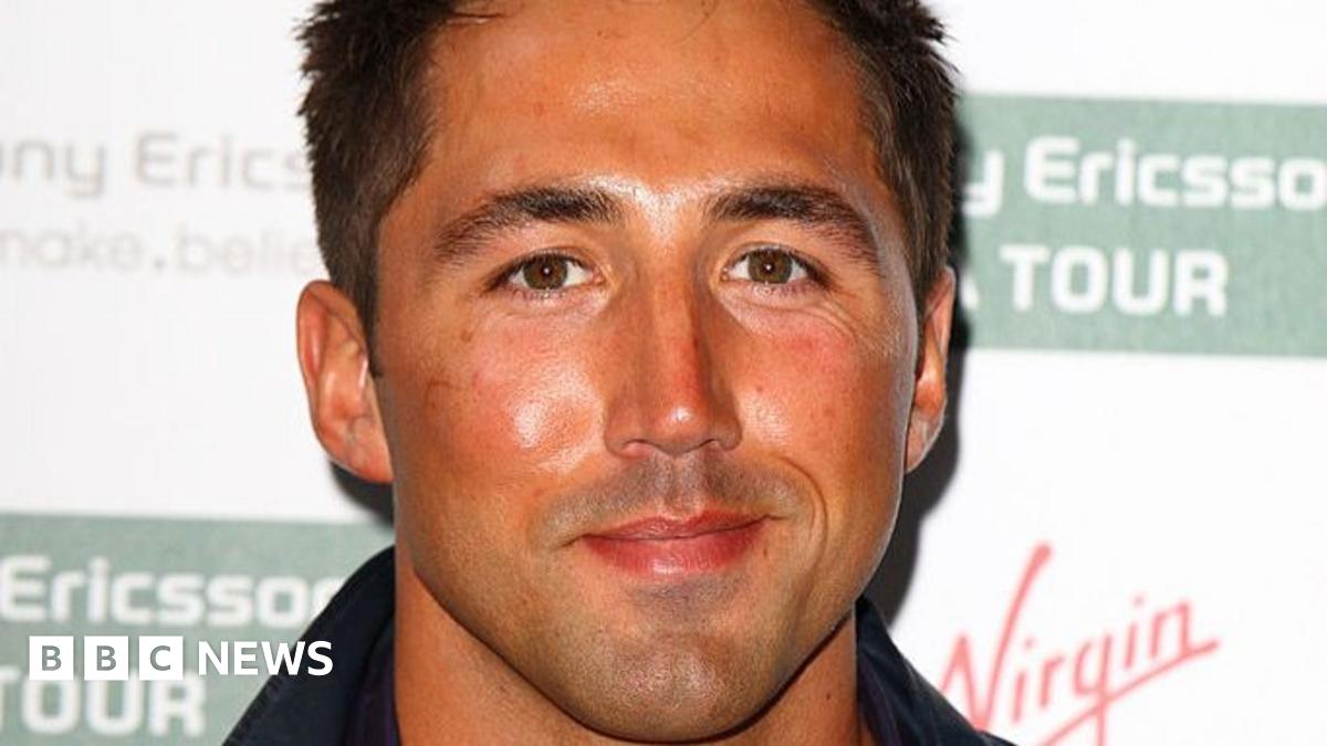 Two woman in front of a green shop, with someone on a ladder in the background. The woman on the left is wearing a blue shirt with brown dots, and the lady on the right is wearing a brown long-sleeve t-shirt.