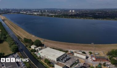 An image made with a drone shows the Chingford Reservoirs in London. A large body of water is surrounded by buildings in the foreground and trees in the background