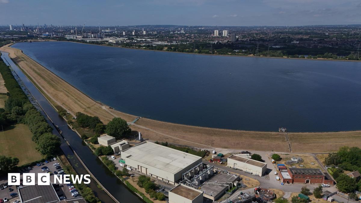 An image made with a drone shows the Chingford Reservoirs in London. A large body of water is surrounded by buildings in the foreground and trees in the background