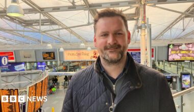 Photograph of Simon Bennett, the station manager at Manchester Piccadilly Station. The image shows the departure board and the platforms in the background.