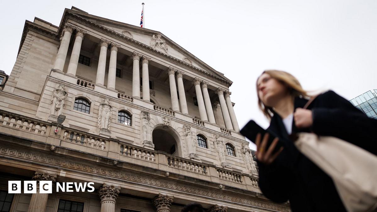 The Bank of England is pictured against a grey sky with people walking in front holding their phones, in Bank, London in December.