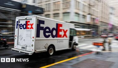 A white van with a purple and orange "FedEx" logo zooms down a city street, which is blurred