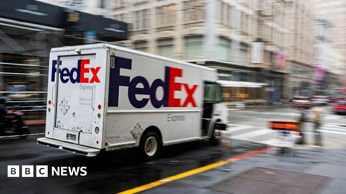 A white van with a purple and orange "FedEx" logo zooms down a city street, which is blurred
