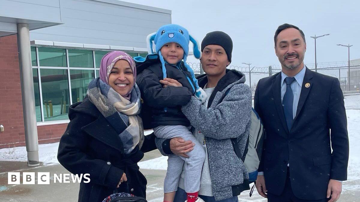 A man holds a five-year-old boy and both are wearing winter hats and smiling, standing outside next to a man and woman who are US congress members
