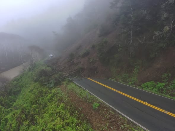 dirt and trees blocking 2 lane highway near the coast