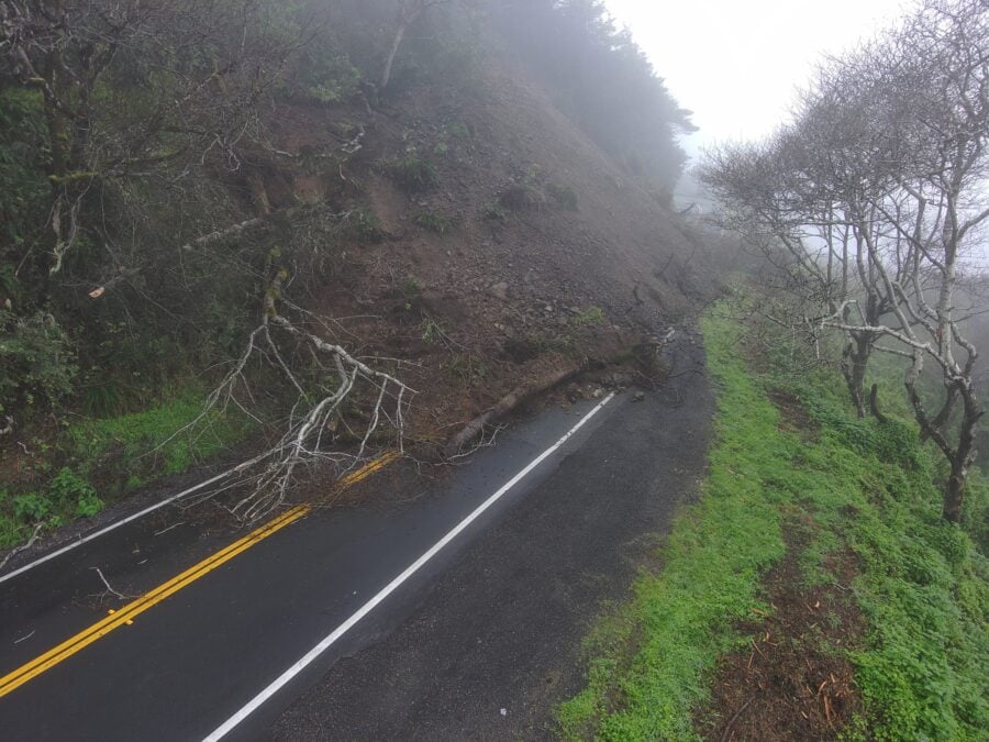 dirt and trees blocking 2 lane highway near the coast