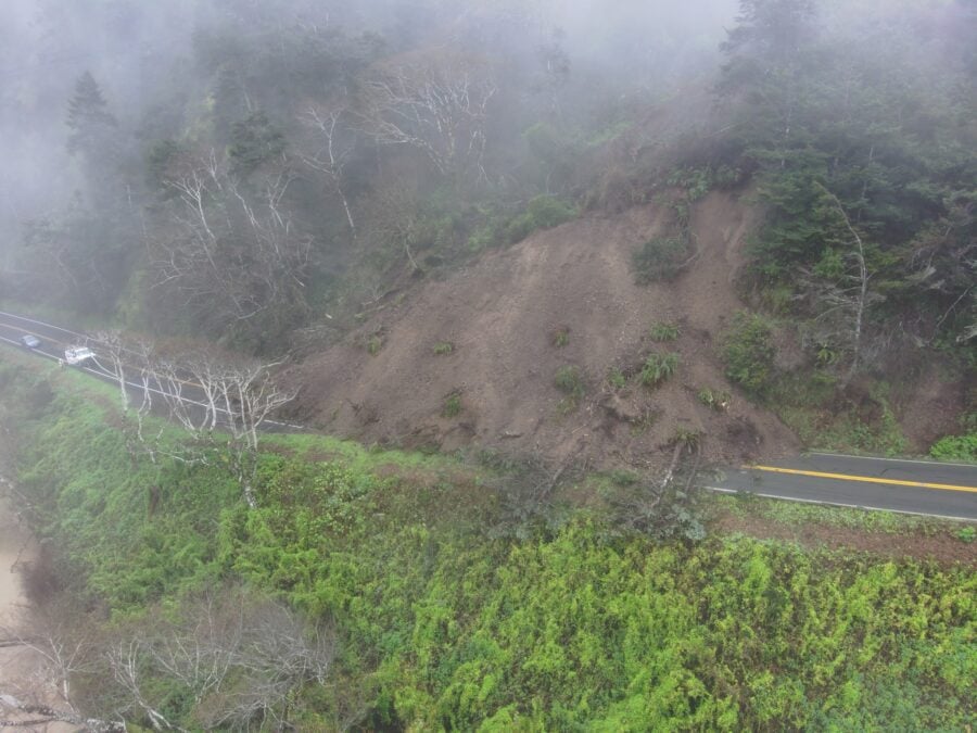 dirt and trees blocking 2 lane highway near the coast