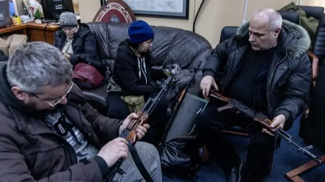 Four people in warm coats check sit on sofas checking rifles