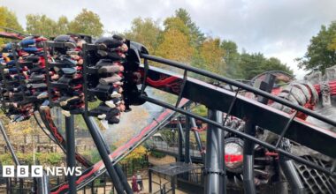 People riding a rollercoaster, their legs dangling underneath the carriage as it speeds at an angle round the track