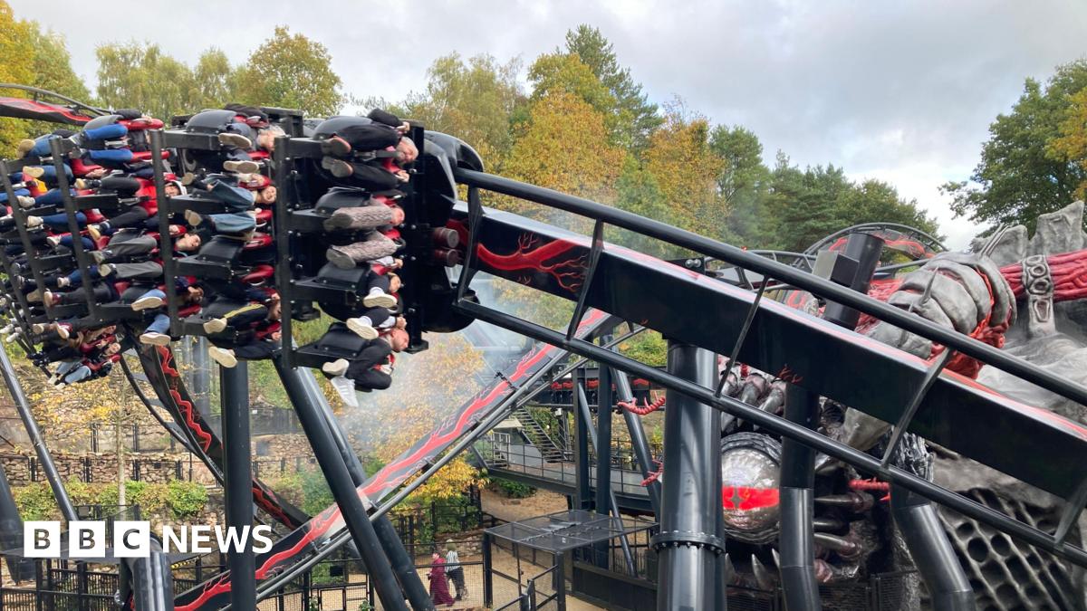 People riding a rollercoaster, their legs dangling underneath the carriage as it speeds at an angle round the track