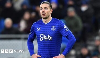 Everton's Jack Grealish stood on a fotball pitch wearing a blue Everton FC shirt with his hands on his hips