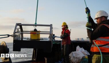 Fayers stood in front of rocks near to the sea. He is wearing a grey jacket and has a grey beard.