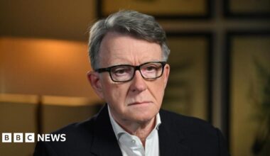 Lord Mandelson sat down wearing a dark suit, white shirt and dark glasses.