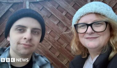 A young man and a middle-aged woman - Noah Herniman and his mother Shelley - stand next to each other next to a garden fence, both wearing beanie hats.