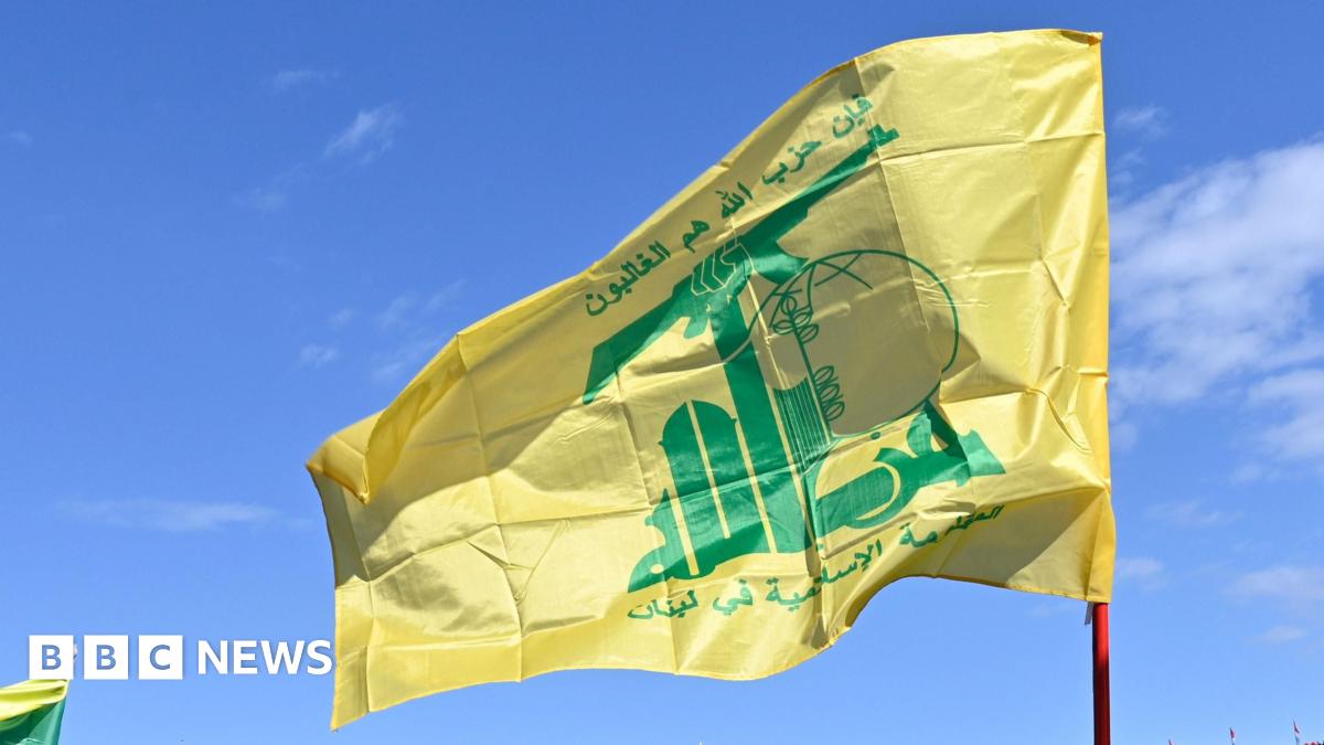 The yellow and green Hezbollah flag flies in the breeze, against a clear blue sky.