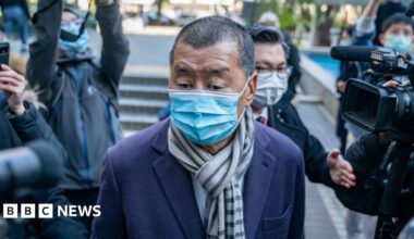 The United Downs power plant in Cornwall is shown, there are various silver pipes surrounding a central plant that has a series of large fan type structures surrounded by yellow pipes. There are trees in the background and the sky is blue.