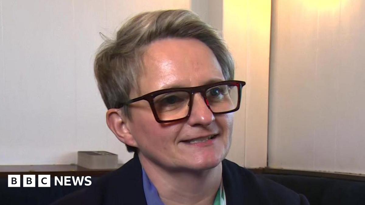 Charlotte Cadden speaks during a TV interview inside a room. She has short fair hair and wears dark glasses.