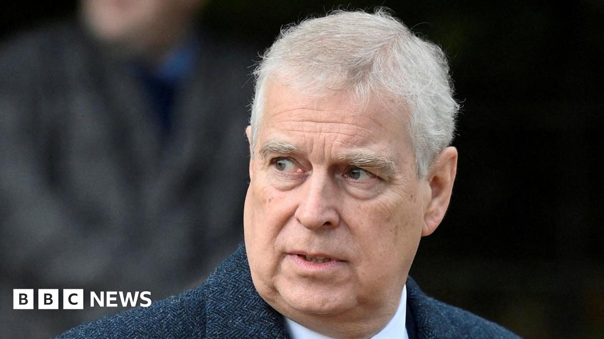 Headshot of Andrew who looks off to the side with his mouth slightly open. The background is blurry but it appears there's a person walking behind him. Taken in December 2022