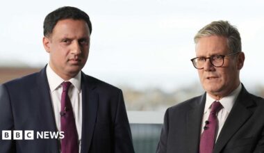 Two  men stand side-by-side posing for a photograph. They are both wearing dark suits, white shirts with ties.