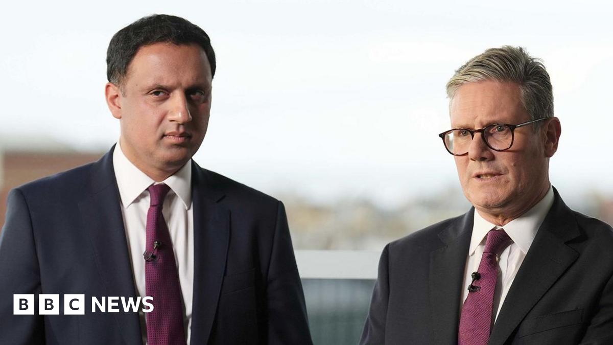 Two  men stand side-by-side posing for a photograph. They are both wearing dark suits, white shirts with ties.