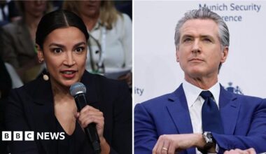 California Governor Gavin Newsom in a royal blue suit and black tie speaks at a conference while holding a microphone and gesturing with his other hand
