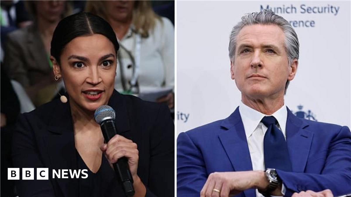 California Governor Gavin Newsom in a royal blue suit and black tie speaks at a conference while holding a microphone and gesturing with his other hand