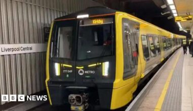 A yellow and black Merseyrail train at a platform at Liverpool Central station. The destination Kirkby is displayed in yellow at the front of the train which carries the Metro logo.