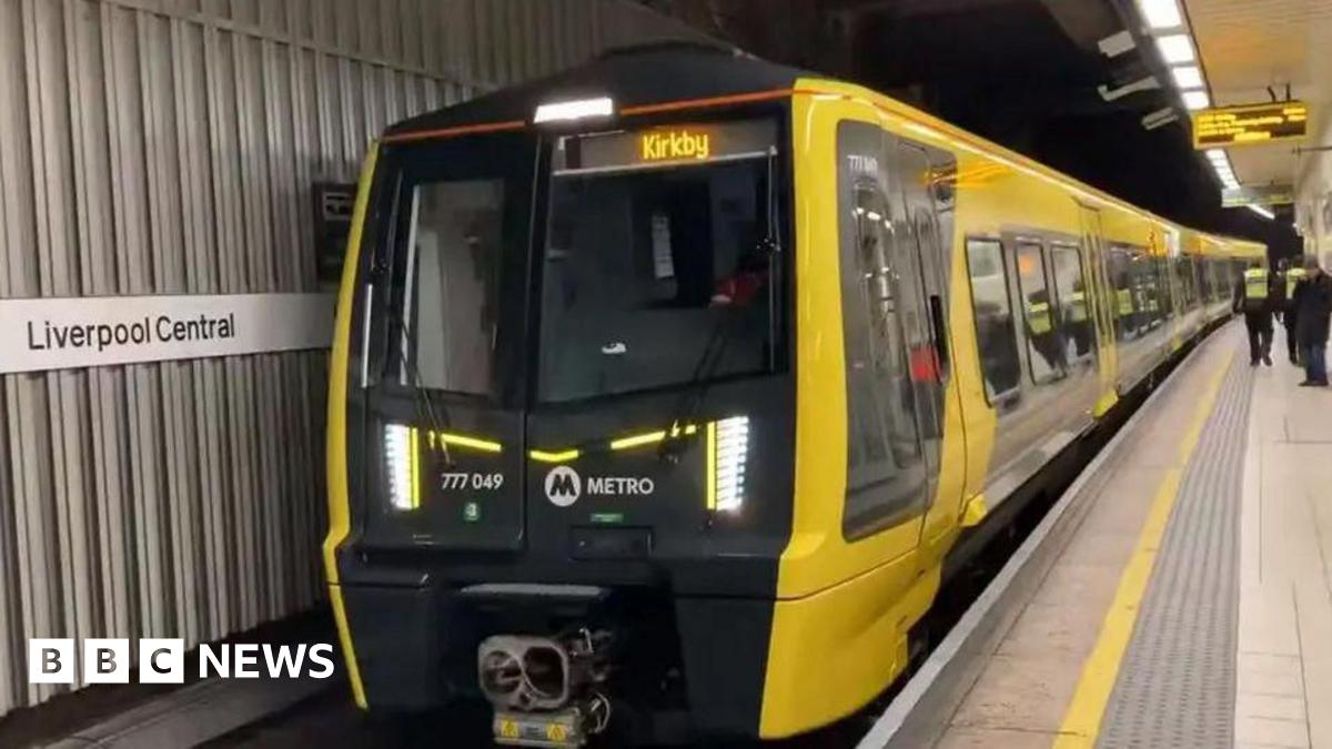 A yellow and black Merseyrail train at a platform at Liverpool Central station. The destination Kirkby is displayed in yellow at the front of the train which carries the Metro logo.