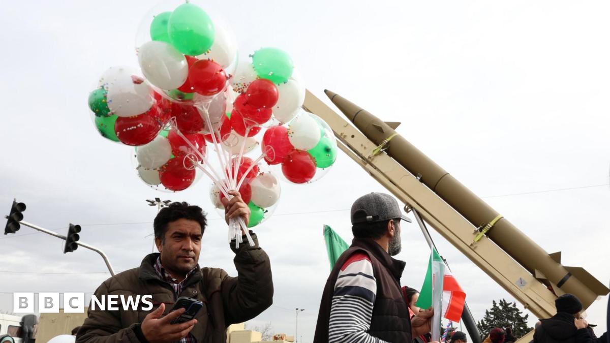 An Iranian man holds up a bunch of green, red and white balloons near a ballistic missile during celebrations marking the 47th anniversary of the Islamic revolution in Tehran, Iran (11 February 2026)