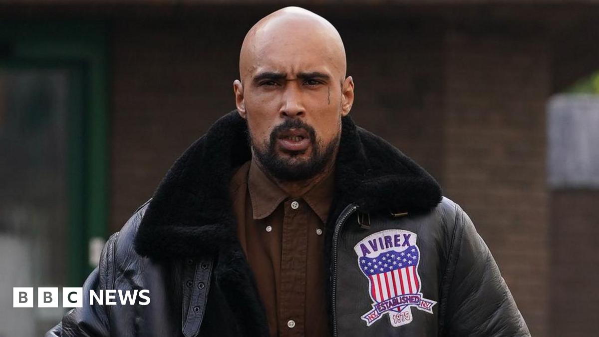 Ashley Warren outside court wearing a brown shirt and a black leather jacket. He is scowling at the camera.