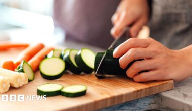 A person at home chops a courgette on a wooden chopping board