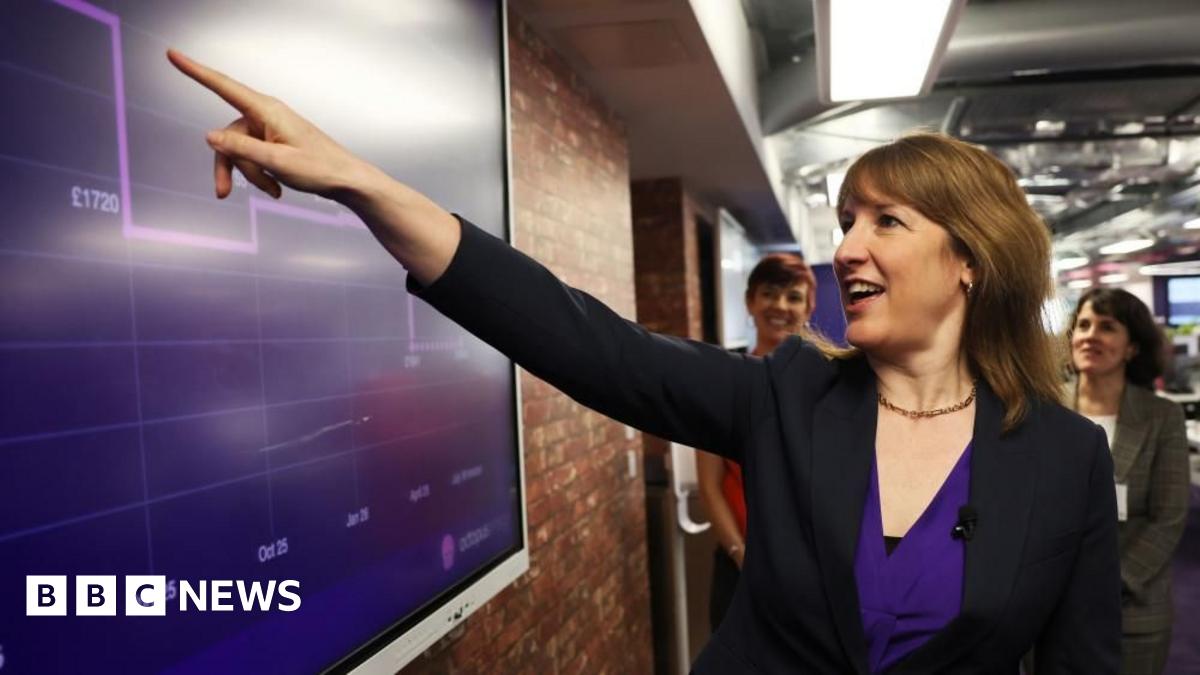 Rachel Reeves smiles while pointing to a large purple chart on a screen,  which shows Octopus energy prices and months. The chart appears to show prices falling.
