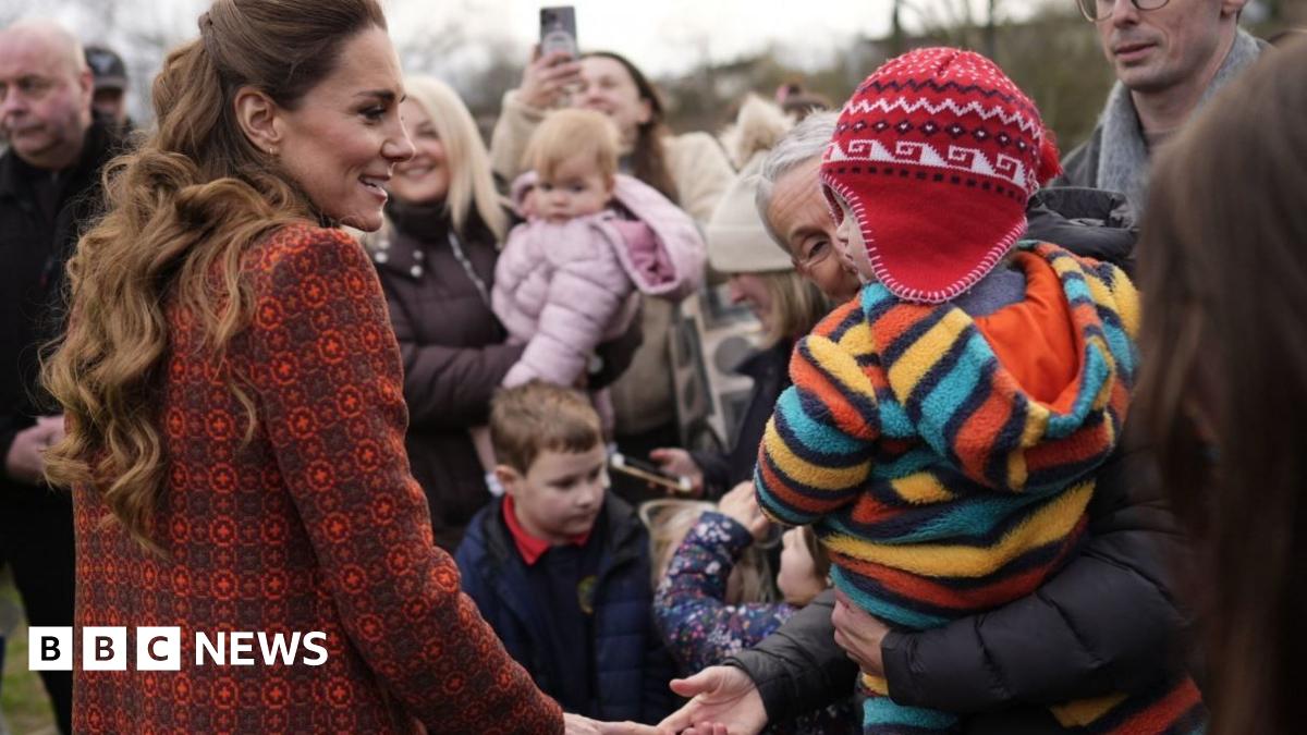 The Princess of Wales is pictured meeting the public outside Hiut Denim. She is wearing a patterned red coat as she greets a small child wearing a colourful fleece and red hat.