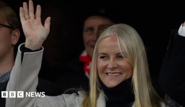 A picture showing a blonde woman in a grey coat and black turtle-neck