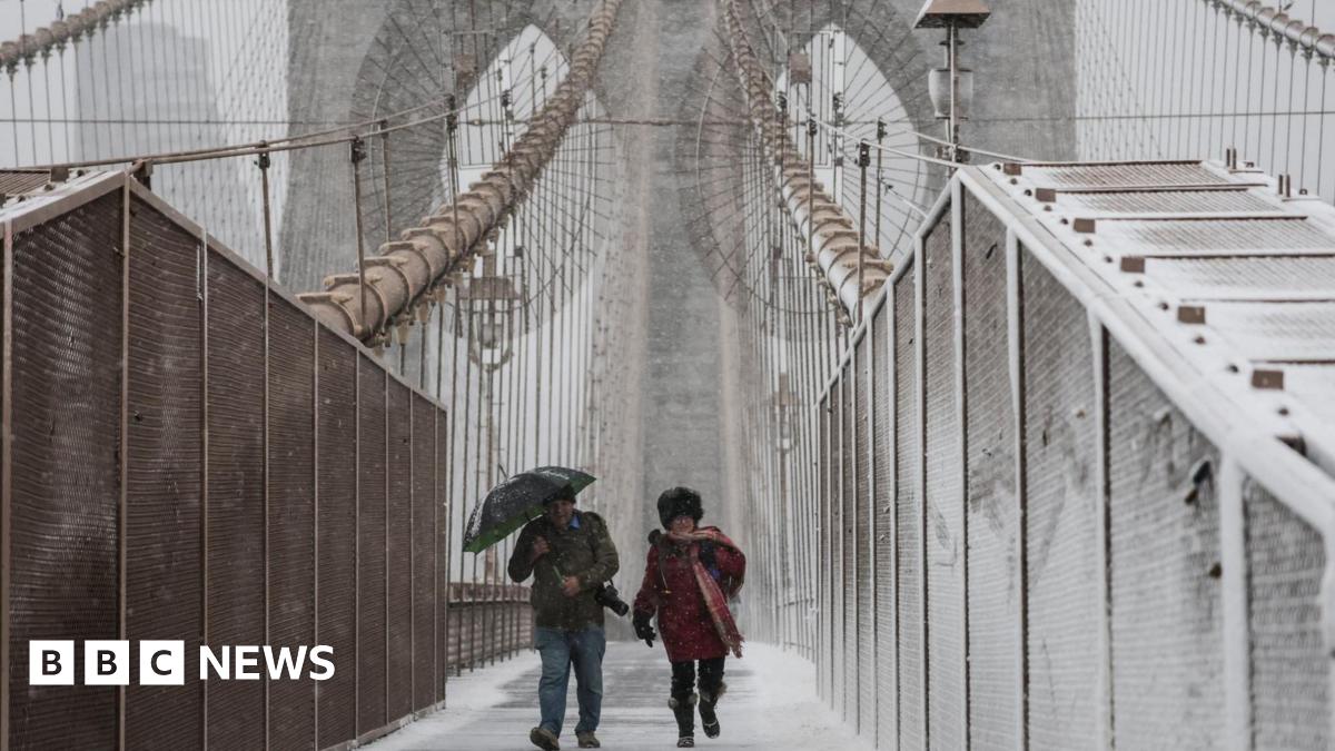 People walk across the Brooklyn Bridge as snow falls during a winter storm in New York Cit on 22 February 2026.