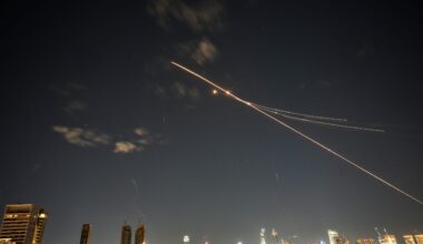 Long-exposure photo of rockets and interceptors crossing the night sky above a city skyline with illuminated buildings.