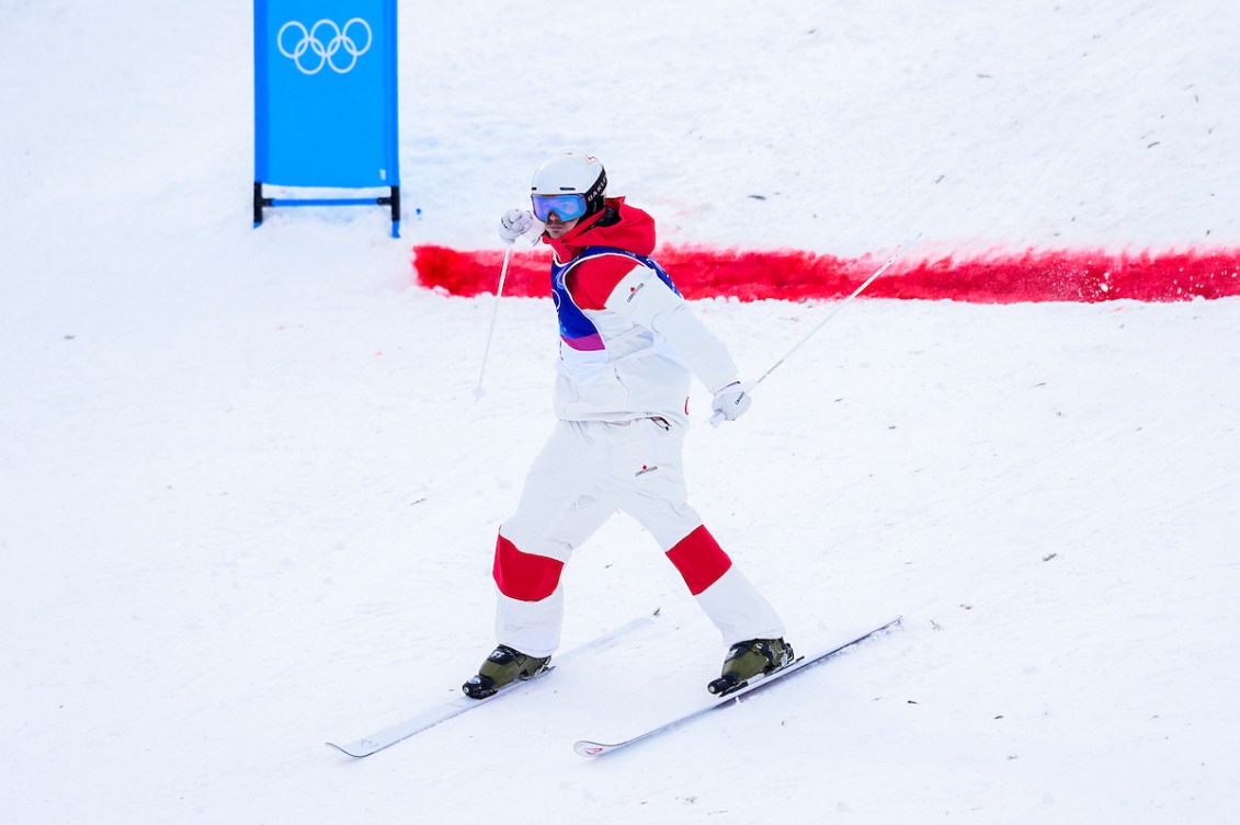 Mikaël Kingsbury of Team Canada celebrates in the finish area after his run in the freestyle ski moguls finals at the Milano Cortina 2026 Olympic Winter Games, reacting with excitement against the snowy course backdrop.