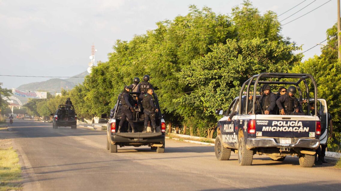 Photo of pickup trucks with police officers in the back driving along a road in Michoacan.