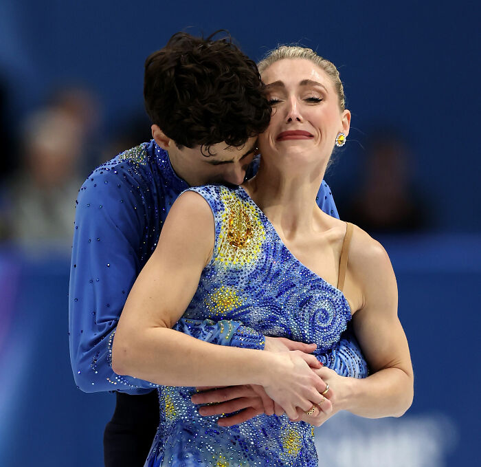 Olympian figure skaters in emotional embrace after judge's conspicuous scores spark cheating accusations controversy.