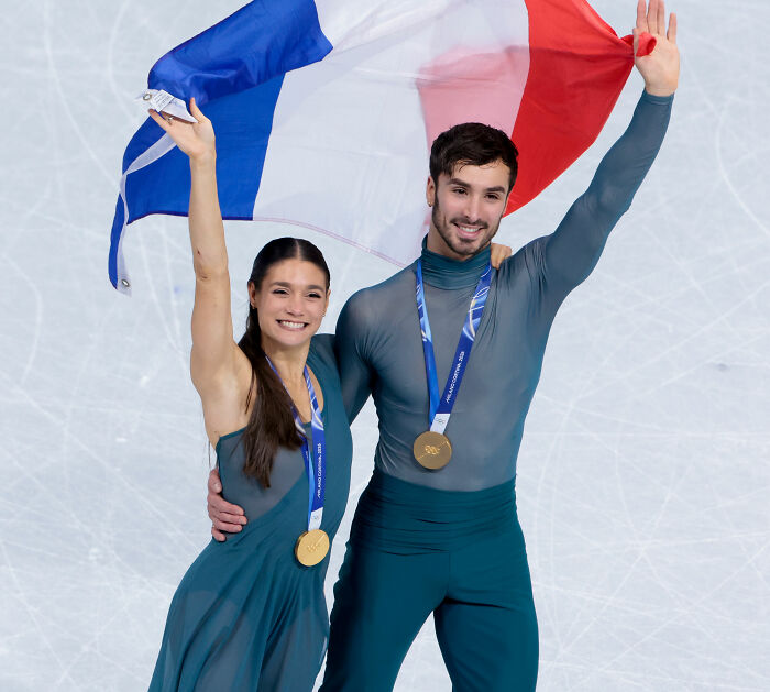 Olympian celebrating with gold medals and French flag after judge's scores sparked cheating accusations at ice skating event.
