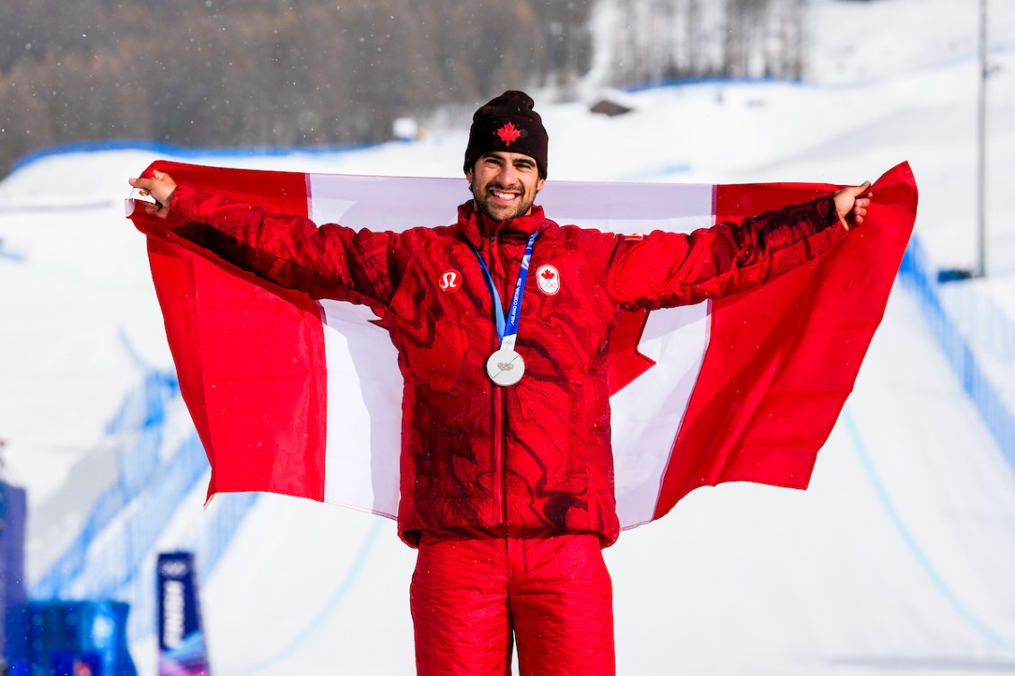 Team Canada’s Éliot Grondin celebrates after winning a silver medal in men’s snowboard cross at the Milano Cortina 2026 Olympic Winter Games, smiling and holding his medal. Photo by Mark Blinch/COC