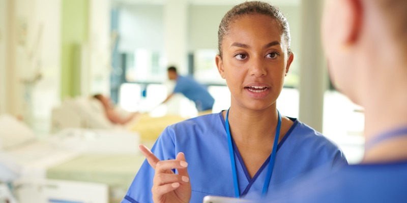 Nursing staff talking with a nurse speaking to a patient in bed in the background