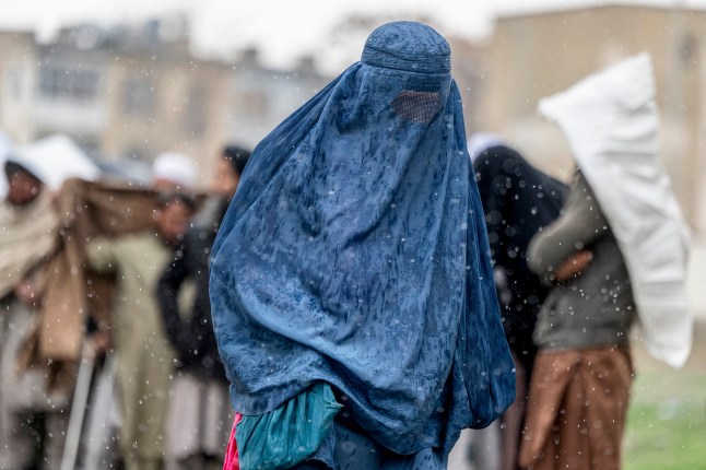 An Afghan burqa-clad woman arrives in the midst of a downpour to receive food supplies donated during the Islamic holy fasting month of Ramadan in Kabul on March 25, 2025. (Photo by Wakil KOHSAR / AFP) (Photo by WAKIL KOHSAR/AFP via Getty Images)