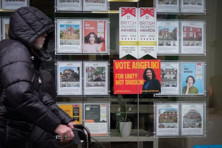 MANCHESTER, UNITED KINGDOM - FEBRUARY 11: A man walks past a campaign poster for labour candidate Angeliki Stogia in an estate agents window in Longsight on February 11, 2026 in Manchester, United Kingdom. A by-election in the Gorton and Denton constituency is scheduled to take place on Thursday, February 26, 2026, triggered by the resignation of former Labour MP Andrew Gwynne due to ill health following his suspension from the party in 2025.??Reform UK is targeting disillusioned voters following Labour's controversial decision to block Greater Manchester Mayor Andy Burnham from standing as their candidate and Nigel Farage has stated the party is in with a "serious shout" to win this traditionally safe Labour seat. Betting odds at the end of January place Reform UK as the favourite at 11/8, followed by the Green Party at 13/8 and Labour at 11/4. (Photo by Christopher Furlong/Getty Images)