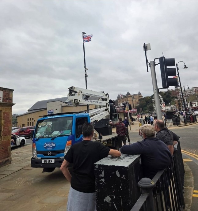 Flags being put up with a cherry picker. // A businessman says he was left "disgusted" after being slapped with a bill of almost ?3,000 for putting up "unauthorised flags". Will Haylett, 43, insists he was only trying to "lift people's spirits" when he hoisted dozens of Union and St George's flags on lampposts around Scarborough, North Yorks., using his company's cherry picker. He did not expect to receive an invoice demanding ?2,785.50 after workers at North Yorkshire Council took them down. Photo released 22/02/2026