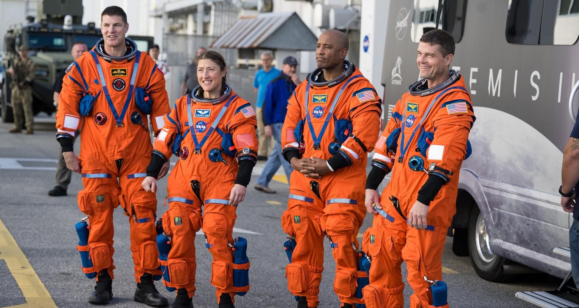 Four people in orange spacesuits stand on a road