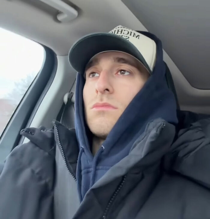 Young man in a winter jacket and cap sitting in a car, showing Canadian hockey fans' reaction after USA wins gold.
